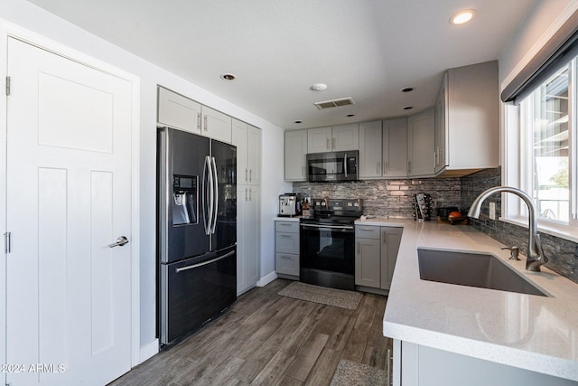 kitchen featuring dark wood finished floors, appliances with stainless steel finishes, a sink, gray cabinetry, and backsplash