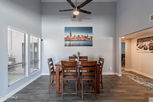 dining space with a towering ceiling, wood finished floors, a ceiling fan, and baseboards