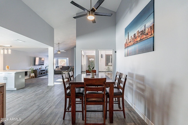 dining space with baseboards, ceiling fan, high vaulted ceiling, and wood finished floors