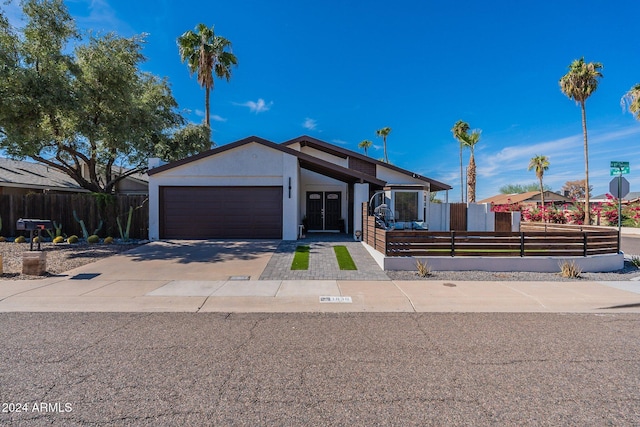 mid-century modern home featuring concrete driveway, a fenced front yard, an attached garage, and stucco siding