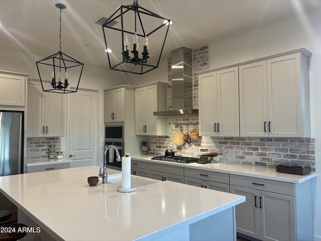 kitchen featuring an island with sink, stainless steel appliances, gray cabinets, and wall chimney range hood