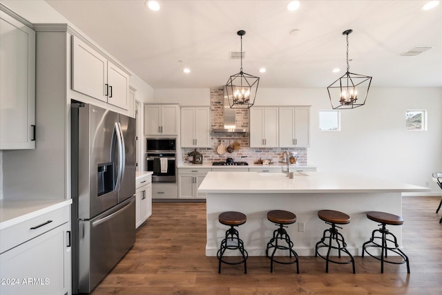 kitchen with appliances with stainless steel finishes, dark hardwood / wood-style floors, a kitchen island with sink, and wall chimney exhaust hood