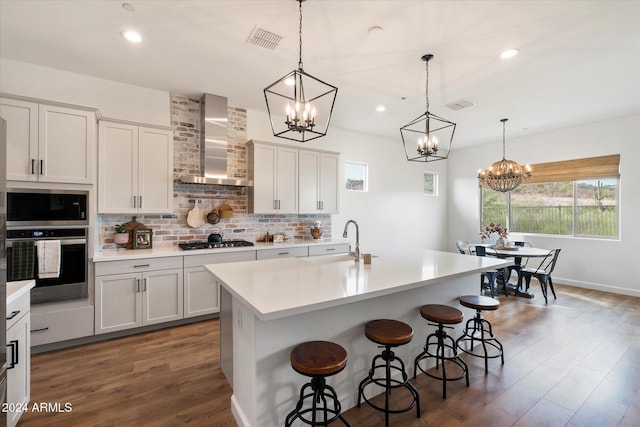 kitchen featuring a center island with sink, pendant lighting, wall chimney range hood, and appliances with stainless steel finishes