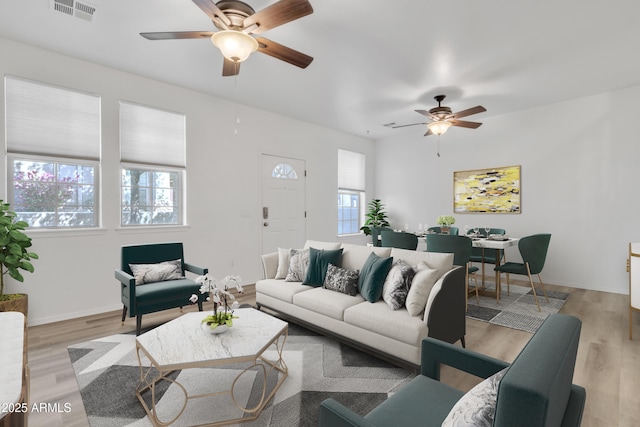 living area with light wood finished floors, baseboards, visible vents, and a ceiling fan