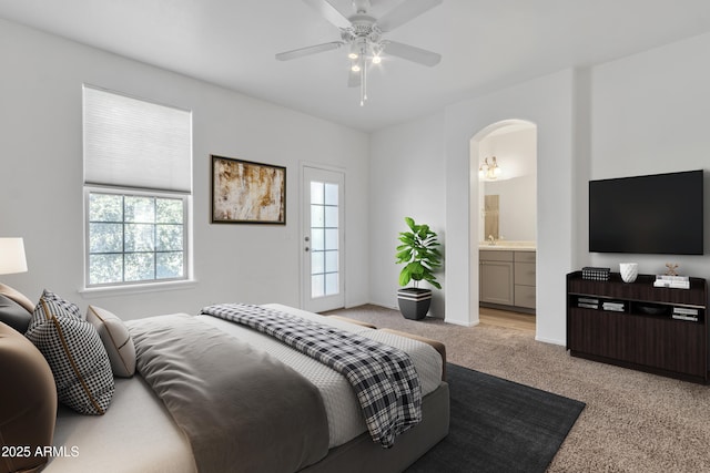 bedroom with light carpet, multiple windows, arched walkways, and connected bathroom