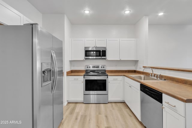 kitchen featuring stainless steel appliances, white cabinetry, a sink, and light wood-style flooring