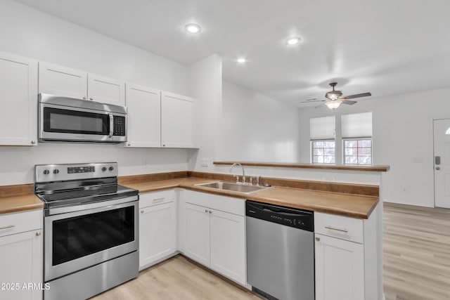 kitchen featuring stainless steel appliances, a peninsula, a sink, white cabinets, and light wood finished floors