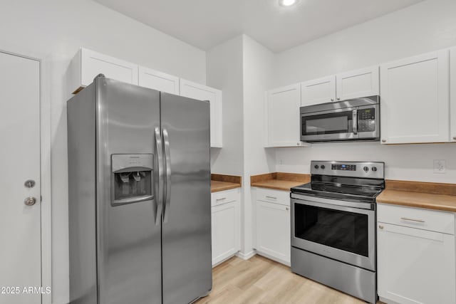 kitchen with appliances with stainless steel finishes, light wood-type flooring, white cabinets, and butcher block countertops