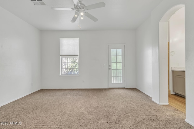 spare room with arched walkways, visible vents, light carpet, ceiling fan, and baseboards