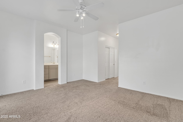 unfurnished bedroom with arched walkways, light carpet, baseboards, a closet, and ensuite bath