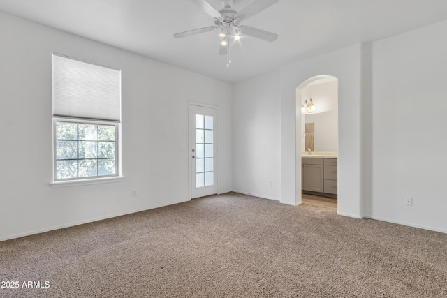 spare room with arched walkways, a ceiling fan, a wealth of natural light, and light colored carpet