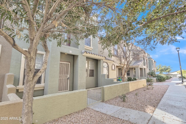 townhome / multi-family property with a fenced front yard, a tiled roof, and stucco siding