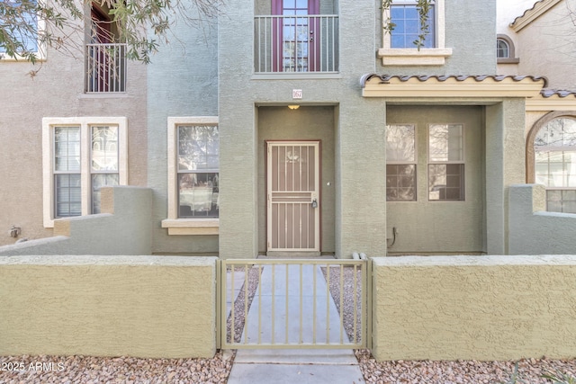 view of exterior entry featuring a gate, a tile roof, and stucco siding