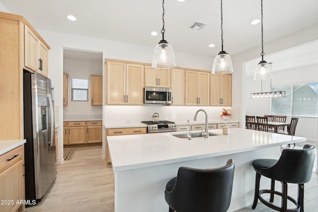 kitchen with pendant lighting, sink, light brown cabinets, stainless steel appliances, and a center island with sink