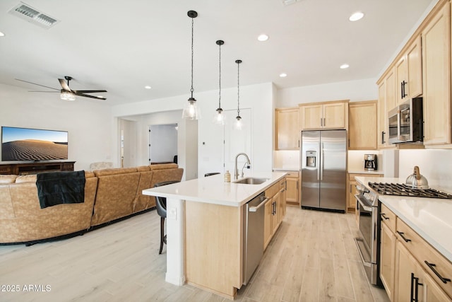 kitchen featuring light brown cabinetry, decorative light fixtures, an island with sink, sink, and stainless steel appliances