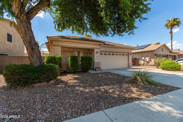 view of front of house featuring a garage, solar panels, fence, driveway, and stucco siding