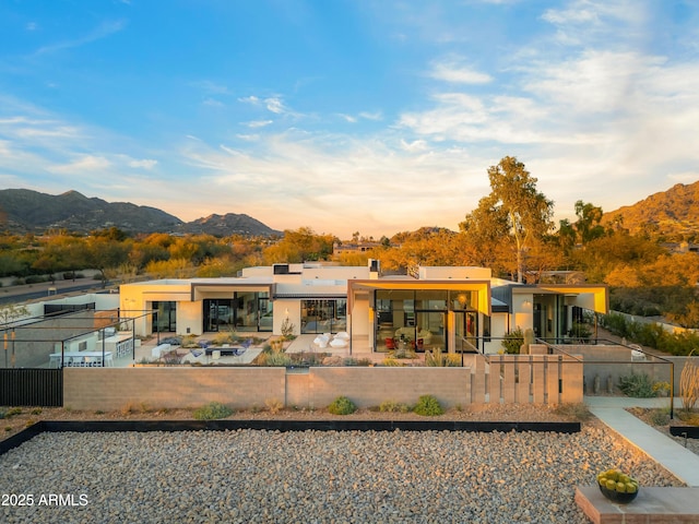 back of property featuring a fenced front yard, a mountain view, a chimney, and stucco siding