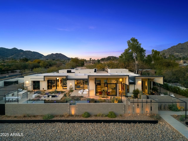 back of house at dusk featuring a patio, fence private yard, a mountain view, and stucco siding