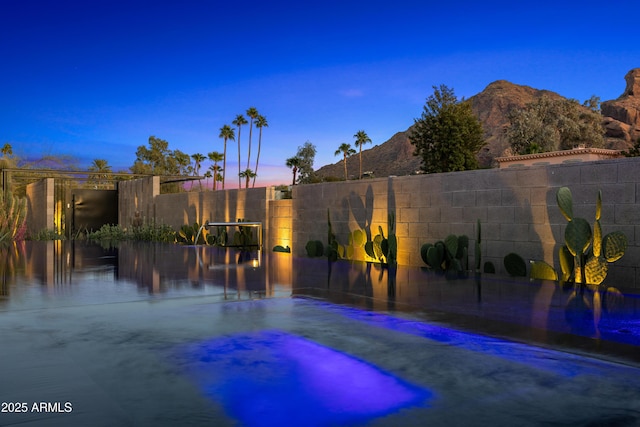 yard at dusk with a hot tub, fence, and a mountain view