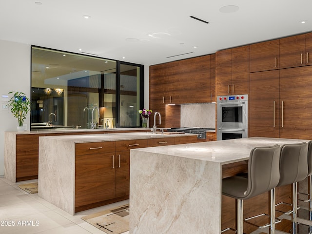 kitchen with light tile patterned floors, stainless steel double oven, brown cabinets, and modern cabinets