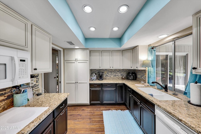 kitchen with white appliances, sink, light stone counters, a tray ceiling, and dark hardwood / wood-style floors