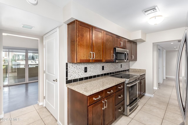 kitchen featuring backsplash, light stone counters, light tile patterned flooring, and appliances with stainless steel finishes