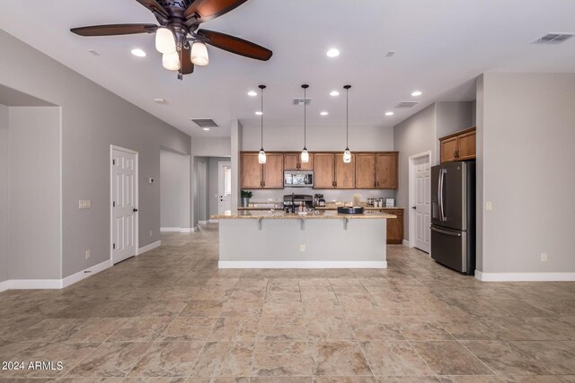 kitchen featuring ceiling fan, light stone counters, pendant lighting, a kitchen island with sink, and appliances with stainless steel finishes