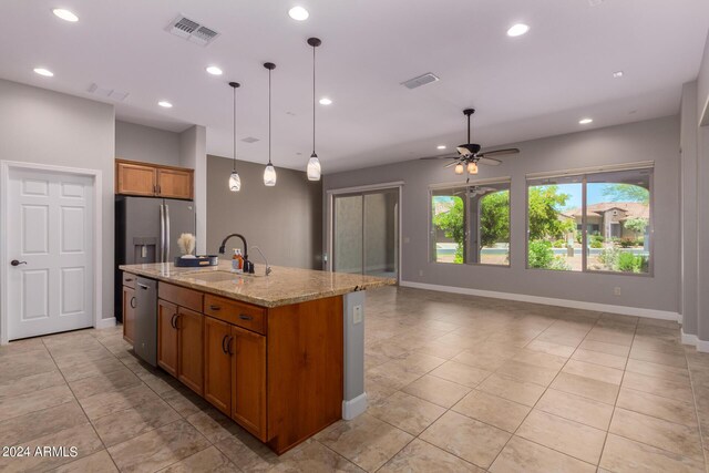 kitchen with light stone counters, stainless steel appliances, ceiling fan, decorative light fixtures, and an island with sink