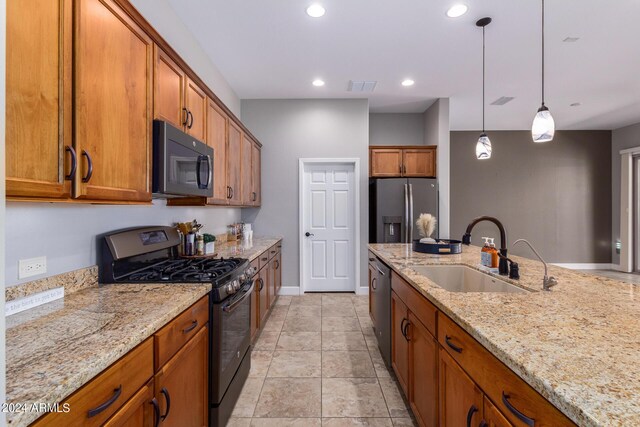 kitchen featuring light stone counters, sink, decorative light fixtures, and appliances with stainless steel finishes