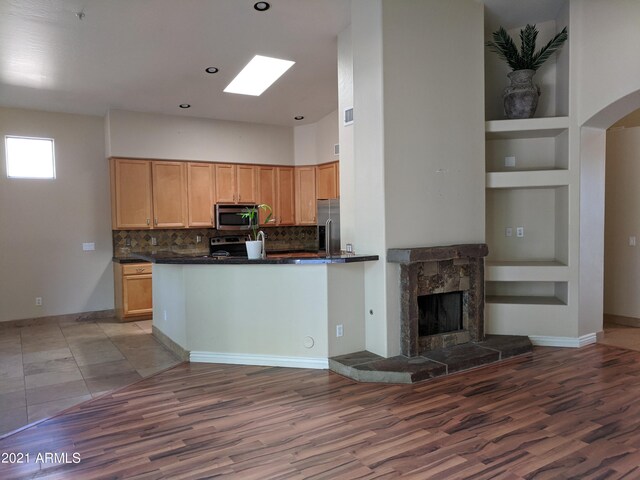 kitchen featuring stainless steel appliances, built in features, tile patterned floors, kitchen peninsula, and a stone fireplace