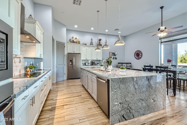 kitchen featuring visible vents, appliances with stainless steel finishes, light wood-style floors, wall chimney exhaust hood, and a sink