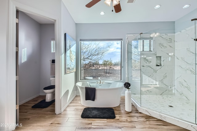 bathroom with wood finished floors, a marble finish shower, a soaking tub, ceiling fan, and toilet