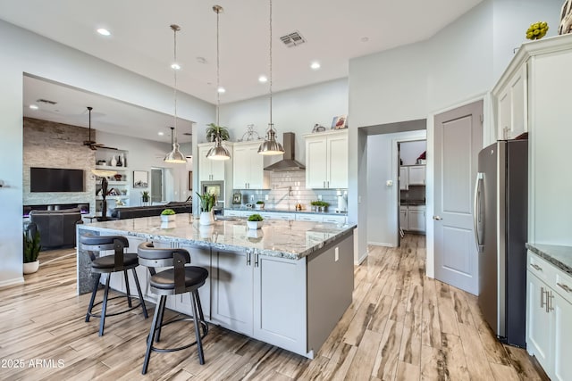 kitchen with visible vents, freestanding refrigerator, open floor plan, wall chimney range hood, and tasteful backsplash