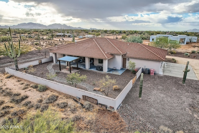 view of front facade with a patio, fence, stucco siding, a tile roof, and a mountain view