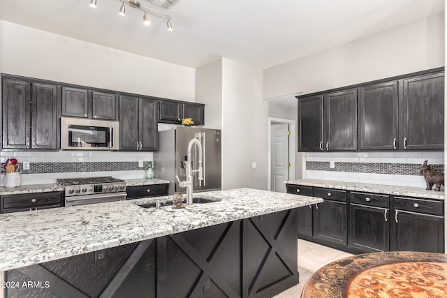 kitchen featuring light stone countertops, tasteful backsplash, an island with sink, light tile patterned flooring, and appliances with stainless steel finishes