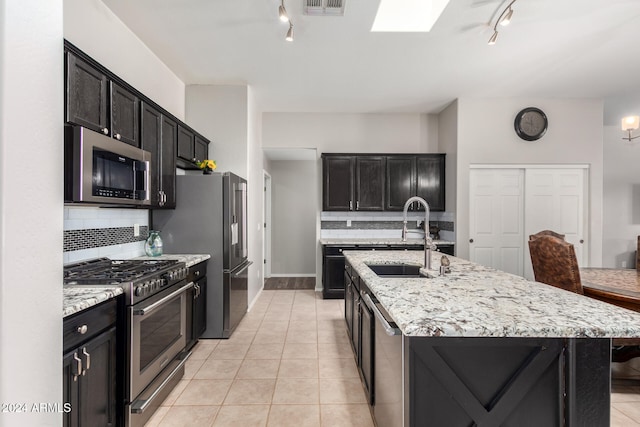 kitchen featuring backsplash, a skylight, high end appliances, sink, and a center island with sink