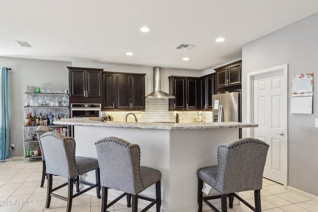 26049 W Matthew Dr, Buckeye, AZ 85396 - kitchen with tasteful backsplash, visible vents, wall chimney range hood, stainless steel appliances, and a breakfast bar area