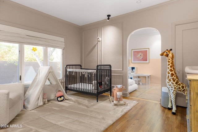 bedroom featuring light hardwood / wood-style floors, crown molding, and a nursery area