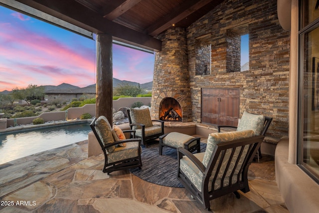 patio terrace at dusk with a fenced in pool and an outdoor stone fireplace