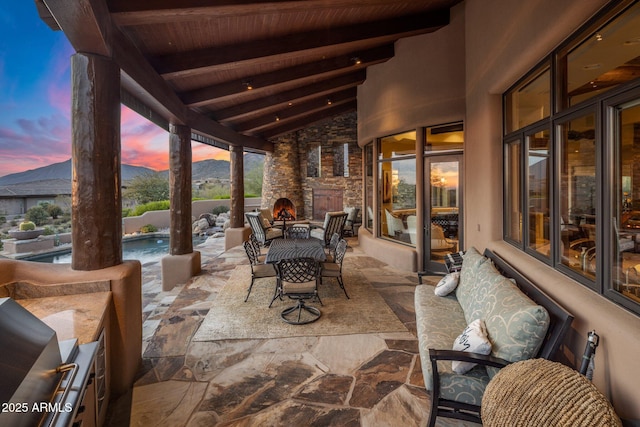 patio terrace at dusk featuring a mountain view and an outdoor stone fireplace