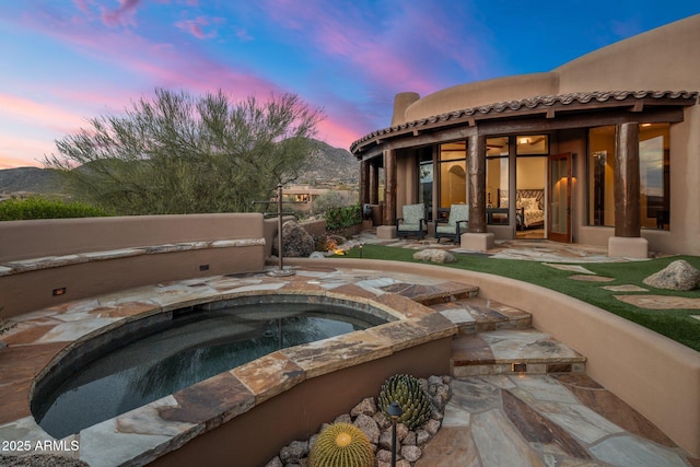 pool at dusk featuring an in ground hot tub, a mountain view, and a patio area