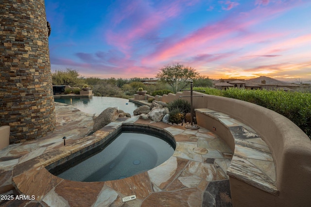 pool at dusk featuring a patio and an in ground hot tub