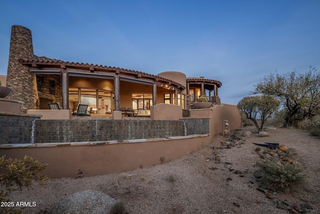 back house at dusk with a fireplace, a balcony, and a patio area