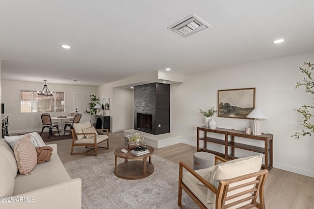 living room with a large fireplace, an inviting chandelier, and light hardwood / wood-style floors