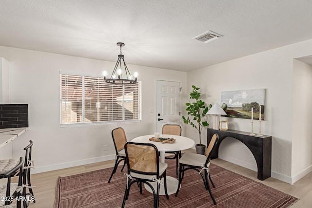 dining area with a textured ceiling, a chandelier, and light hardwood / wood-style flooring