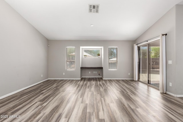 unfurnished room featuring baseboards, visible vents, wood finished floors, and vaulted ceiling