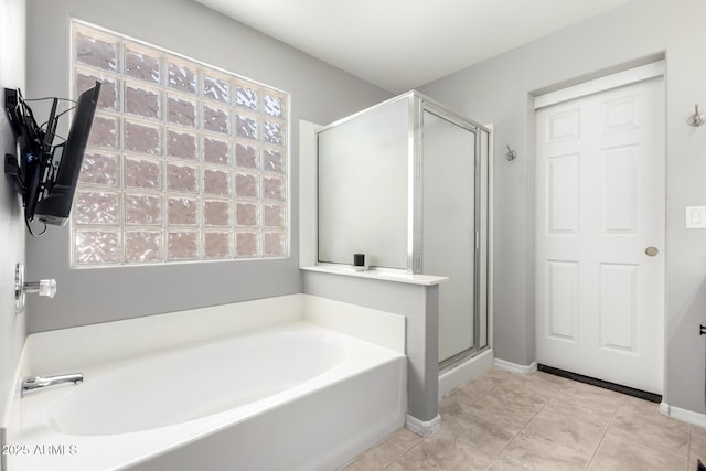 bathroom featuring tile patterned floors, a bath, a stall shower, and baseboards