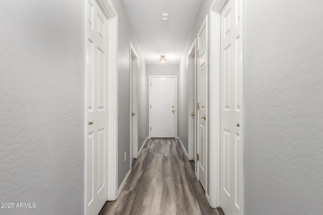 hall featuring a textured wall, dark wood finished floors, and baseboards