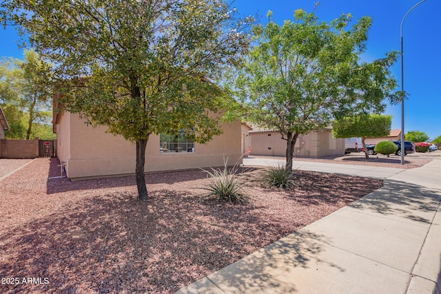 view of property hidden behind natural elements with stucco siding, fence, and driveway