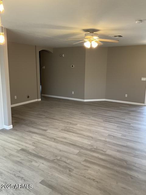 spare room featuring arched walkways, a ceiling fan, baseboards, and wood finished floors
